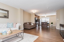 Open-concept living space featuring wood-finish flooring, a kitchen island with seating, stainless steel appliances, and ceiling-mounted light fixtures - 