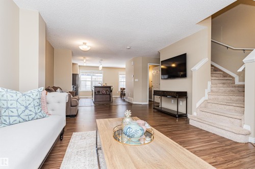 Open-concept living space featuring wood-finish flooring, a carpeted staircase with white railings, and neutral wall tones - 31 4029 Orchards Drive, Edmonton, AB 