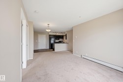 Open-concept living area with neutral carpeting, leading to a kitchen featuring dark cabinetry and black appliances - 