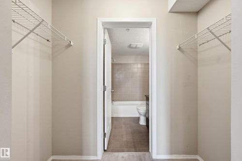 Alcove with light neutral wall paint and white wire shelving, opening to a bathroom with a white tub and tiled walls - 304 11804 22 Avenue, Edmonton, AB 