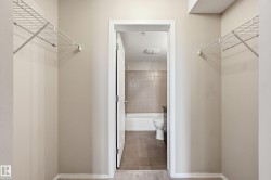 Alcove with light neutral wall paint and white wire shelving, opening to a bathroom with a white tub and tiled walls - 