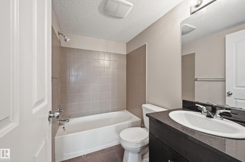 Bathroom featuring a white bathtub, tiled shower surround, dark vanity with an integrated sink, and a wall-mounted mirror - 304 11804 22 Avenue, Edmonton, AB 