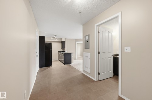 Open-concept living space featuring ceramic tile flooring, a black refrigerator, dark cabinetry, and a track lighting fixture - 304 11804 22 Avenue, Edmonton, AB 