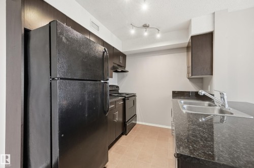Kitchen featuring dark wood-finish cabinetry, black appliances, a double basin sink, and track lighting - 304 11804 22 Avenue, Edmonton, AB 