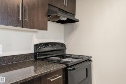 Kitchen featuring dark wood-finish cabinetry with silver hardware, speckled dark countertops, and a black electric range with an overhead vent - 