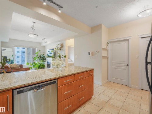 Kitchen island featuring a light-toned countertop, wood-finish cabinetry, and an integrated stainless steel dishwasher - 409 10333 112 Street, Edmonton, AB 