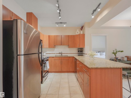 Kitchen featuring wood-finish cabinetry, stainless steel appliances, speckled stone countertops, and tile flooring - 409 10333 112 Street, Edmonton, AB 