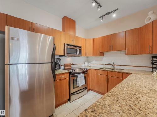 Kitchen featuring light wood cabinetry, stainless steel appliances, granite countertops, white subway tile backsplash, and track lighting - 409 10333 112 Street, Edmonton, AB 