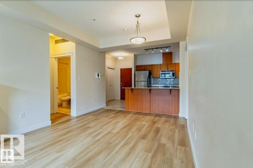 Bright living space featuring wood-finish flooring and a tray ceiling with a hanging fixture - 409 10333 112 Street, Edmonton, AB 