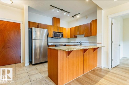 Kitchen featuring wood cabinetry, stainless steel appliances, granite countertops, a subway tile backsplash, and tile flooring - 409 10333 112 Street, Edmonton, AB 