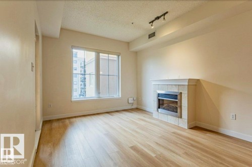 Living area featuring wood-finish flooring, a window with multiple panes, a built-in fireplace with a tiled surround, and track lighting - 409 10333 112 Street, Edmonton, AB 