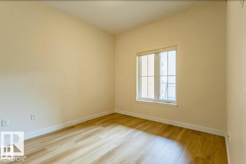 Bright room featuring a large window with vertical mullions, wood-finish flooring, and light-toned walls - 409 10333 112 Street, Edmonton, AB 