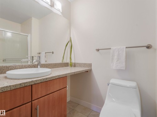 Bathroom featuring a contemporary vessel sink, chrome faucet, wood-finish vanity cabinetry, and a light-toned granite countertop - 409 10333 112 Street, Edmonton, AB 