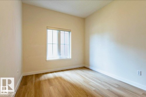 Room featuring a vaulted ceiling, wood-finish flooring, and a large window with white trim - 409 10333 112 Street, Edmonton, AB 