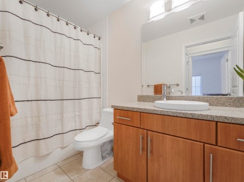 Contemporary bathroom featuring a light wood-finish vanity with brushed nickel hardware, a speckled stone countertop, and a white vessel sink with a chrome faucet - 409 10333 112 Street, Edmonton, AB 