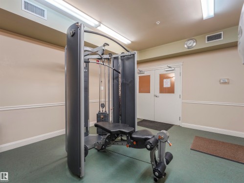 Dedicated fitness area featuring a multi-station exercise machine, neutral wall tones with chair rail molding, and a textured green floor - 409 10333 112 Street, Edmonton, AB 