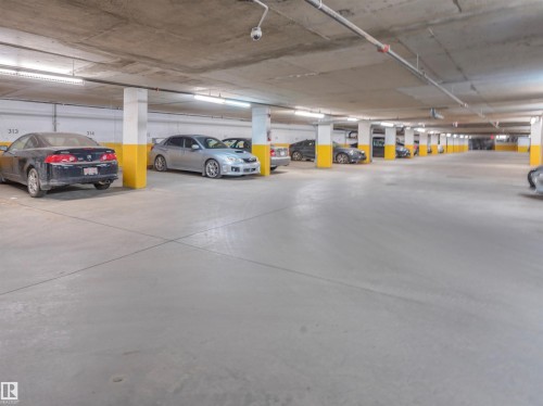 Underground parking garage featuring concrete flooring and ceiling, white support columns with yellow accents, and overhead fluorescent lighting - 409 10333 112 Street, Edmonton, AB 