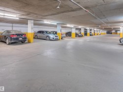 Underground parking garage featuring concrete flooring and ceiling, white support columns with yellow accents, and overhead fluorescent lighting - 