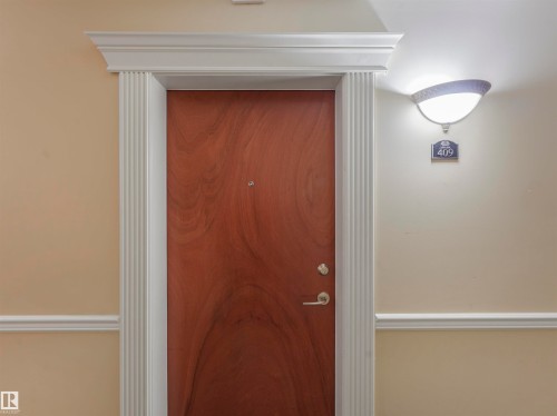 Entry door with fluted casing and crown molding, satin nickel hardware, and an overhead wall sconce - 409 10333 112 Street, Edmonton, AB 