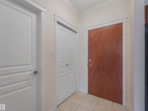 Entryway featuring a wood-finish door with brushed nickel hardware, light-toned tile flooring, and white trim - 409 10333 112 Street, Edmonton, AB 
