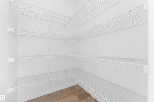 Walk-in pantry featuring white wire shelving, extending along multiple walls, and wood-finish flooring - 1534 157 Street, Edmonton, AB 