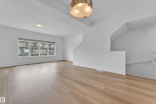 Spacious interior featuring wide-plank wood-finish flooring, a large multi-pane window, bright white walls, recessed ceiling lighting, and a contemporary semi-flush mount fixture - 1534 157 Street, Edmonton, AB 
