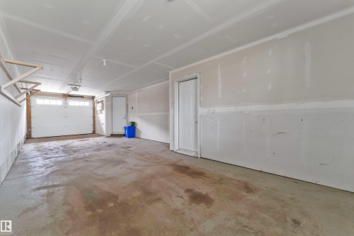 Spacious garage featuring a concrete floor, overhead lighting, an overhead garage door with upper window panels, and an interior access door - 1534 157 Street, Edmonton, AB 