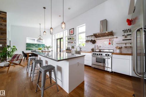 Open-concept kitchen featuring an oversized island with seating, stainless steel appliances, white subway tile backsplash, wood-finish countertops, and hardwood flooring - 14508 78 Avenue, Edmonton, AB 