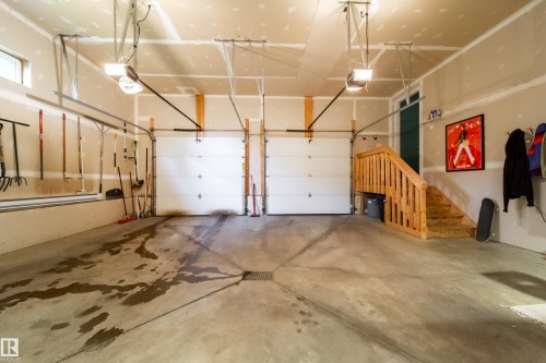 Two-car garage featuring concrete flooring, dual automatic garage doors, and a wood staircase providing interior access - 14508 78 Avenue, Edmonton, AB 