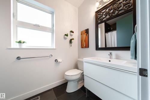 Bathroom featuring a white floating vanity with an integrated sink, a large ornate framed mirror, and dark tile flooring - 14508 78 Avenue, Edmonton, AB 