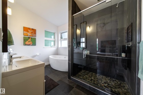 Modern bathroom featuring a frameless glass shower enclosure with pebble flooring, a freestanding soaking tub, and a white vanity with an integrated sink - 14508 78 Avenue, Edmonton, AB 