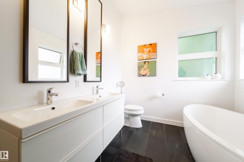 Modern bathroom featuring a dual vanity, dark tile flooring, a freestanding soaking tub, and a window for natural light - 14508 78 Avenue, Edmonton, AB 