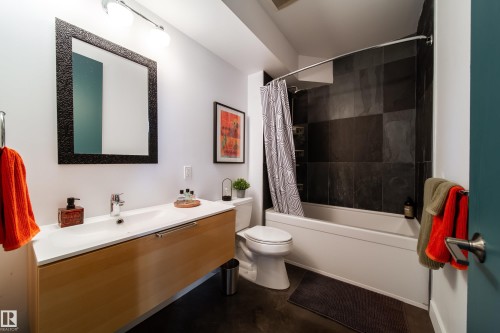 Bathroom featuring a floating wood-finish vanity with an integrated white sink, a rectangular framed mirror, and a wall-mounted light fixture - 14508 78 Avenue, Edmonton, AB 