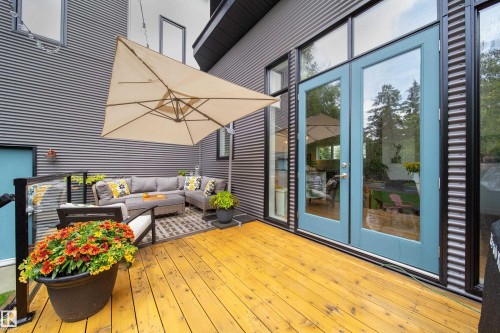 Expansive wood-finish deck with glass railing, providing access to the interior via light blue double doors - 14508 78 Avenue, Edmonton, AB 