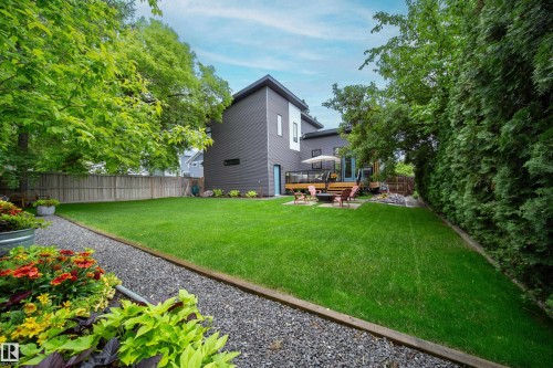 Expansive backyard featuring a manicured lawn, a gravel pathway, and a wooden deck with a modern grey siding structure - 14508 78 Avenue, Edmonton, AB 