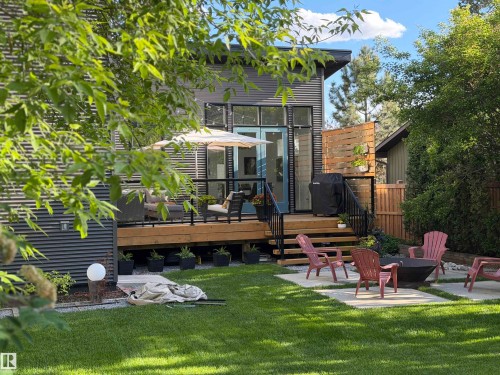 Expansive backyard featuring a manicured lawn, a concrete paver patio with a central fire pit, and a wooden deck with black railings - 14508 78 Avenue, Edmonton, AB 