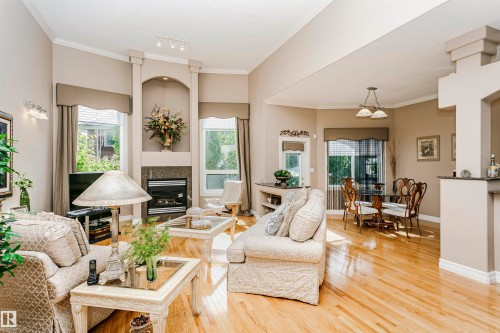 Spacious living area featuring high ceilings, light wood-finish flooring, and a gas fireplace with a stone surround - 116 Darlington Crescent, Edmonton, AB 