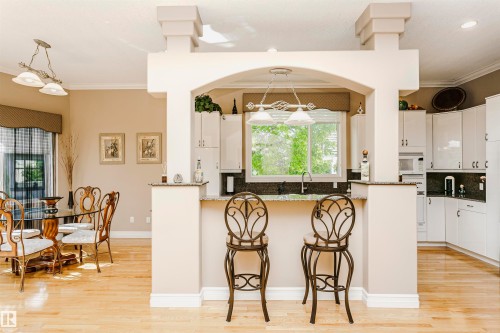 Open-concept kitchen and dining area featuring light wood-finish flooring, a kitchen island with seating, white cabinetry, and dark countertops - 116 Darlington Crescent, Edmonton, AB 