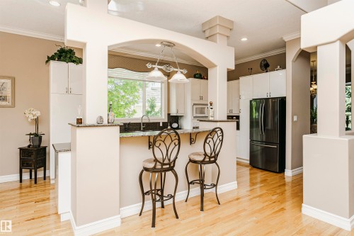 Open-concept kitchen with light wood-finish flooring, white cabinetry, dark stone countertops, and a black French door refrigerator - 116 Darlington Crescent, Edmonton, AB 