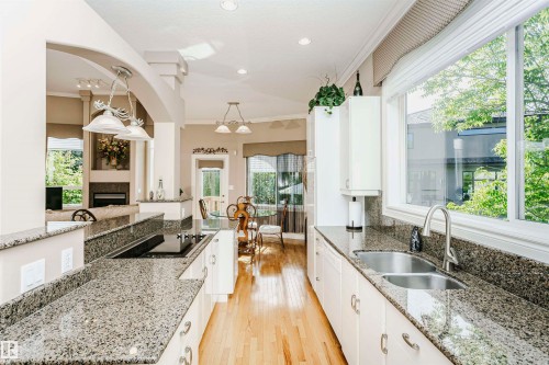 Open-concept kitchen featuring granite countertops, light wood-finish flooring, a built-in cooktop, and an undermount double-basin sink - 116 Darlington Crescent, Edmonton, AB 