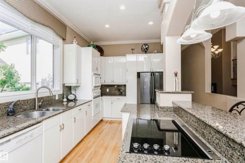 Bright kitchen featuring a window over a double-basin stainless steel sink, granite countertops, light wood-finish flooring, white cabinetry, and stainless steel appliances - 116 Darlington Crescent, Edmonton, AB 
