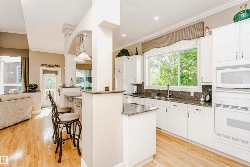 Open-concept kitchen featuring white cabinetry, granite countertops, and wood-finish flooring - 116 Darlington Crescent, Edmonton, AB 