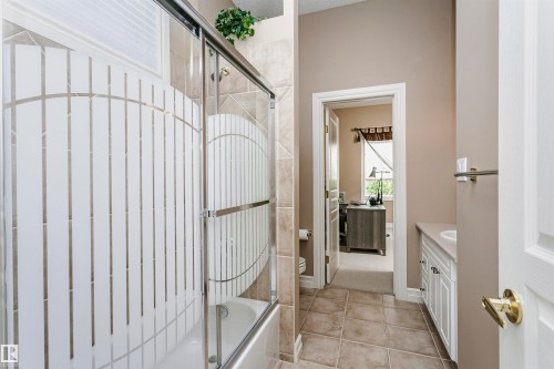 Bathroom featuring a tub/shower combination with patterned frosted glass enclosure, tiled surround, and tiled flooring - 116 Darlington Crescent, Edmonton, AB 