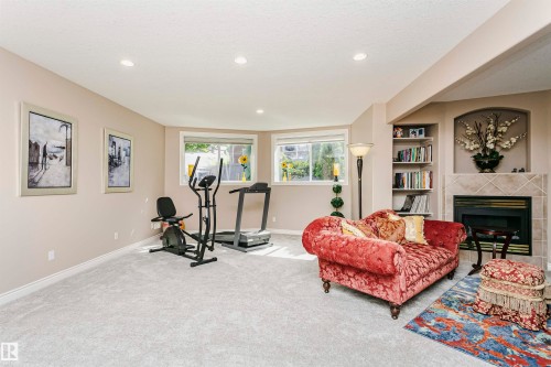 Spacious room featuring light gray carpeting, recessed lighting, a fireplace with a tiled surround and hearth, multiple windows, and built-in shelving - 116 Darlington Crescent, Edmonton, AB 