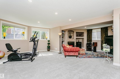 Spacious entertainment area featuring recessed lighting, light-toned carpet, built-in shelving, a fireplace with a stone surround, and multiple windows - 116 Darlington Crescent, Edmonton, AB 