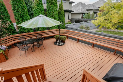 Expansive wood-finish deck featuring integrated bench seating, built-in planter boxes, and perimeter evergreen trees - 116 Darlington Crescent, Edmonton, AB 
