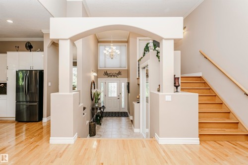 Grand entryway featuring an arched column structure, wood-finish flooring, a wood staircase with a natural wood handrail, a chandelier, and a double entry door with decorative glass - 116 Darlington Crescent, Edmonton, AB 