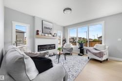Spacious living area featuring light wood-finish flooring, a contemporary linear electric fireplace with a wood mantle, and extensive natural light through large windows - 