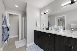 Bathroom featuring a dual vanity with a light-toned countertop, dark wood-finish cabinetry, and a full-width mirror - 