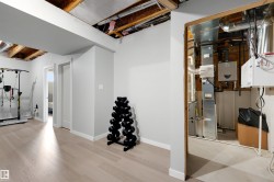 Finished basement space featuring light wood-finish flooring, white walls, and exposed ceiling joists - 
